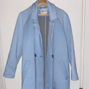 Ljusblå kappa från ONLY, storlek S - Snygg ljusblå kappa från ONLY i storlek S. Klassisk rak modell med krage, två knappar framtill och praktiska fickor. Materialet känns mjukt och har en stilren look som passar till många outfits. Knappt använd!