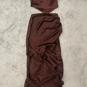 Matching ser från ASOS DESIGN - Snygg mörkröd långklänning från ASOS DESIGN i glansigt satintyg. Klänningen har en figurnära passform med ärmlös bandeau-topp och lång, svepande kjol. Perfekt för dig som vill sticka ut med en elegant och trendig look.