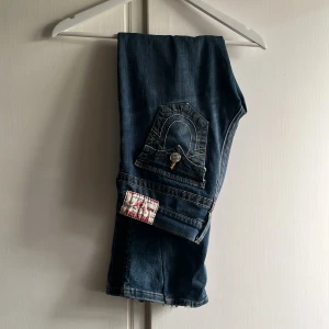 True Religion blå bootcut jeans - Pris går att diskutera!! Säljer ett par klassiska blå jeans från True Religion med tydliga kontrastsömmar och ikonisk fickdetalj bak. Modellen har bootcut-ben och väldigt låg midja. Jeansen är i denim med snygg tvätt och har detaljer som nitar och logotyp-patch. Säljer på grund av att dom inte kommer till användning.