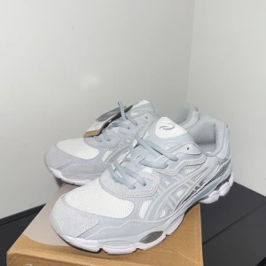 Asics GEL NYC gray/white  - Snygga Asics sneakers i vitt och ljusgrått med mesh och syntetdetaljer. Skorna har klassisk snörning, rund tå och platt sula. Perfekta för dig som gillar sportig stil och vill ha bekväma skor till vardagen. Asics-logga på sidan och tungan. Pris går naturligtvist att diskutera. Skorna är helt nya.