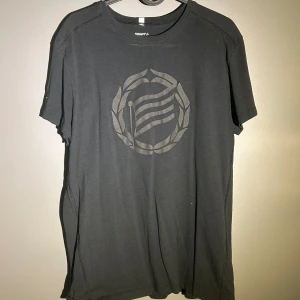 Hammarby tshirt - Svart t-shirt från Craft med rund hals och korta ärmar. Framsidan har ett stilrent tryck med en krans och vågiga linjer. Skön passform och mjukt material, perfekt för chill eller sportiga dagar.