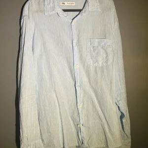 Ljusblå linneskjorta från Zara - Snygg ljusblå skjorta från Zara i luftigt linne. Klassisk krage, bröstficka och knäppning framtill. Perfekt för en chill och stilren look, passar lika bra till jeans som shorts.