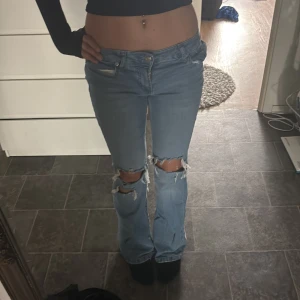 Ljusblå bootcut jeans med hål - Säljer ett par ljusblå jeans med bootcut-modell och snygga slitningar över knäna. Lite slitna längst ner.Xxs/xs. 