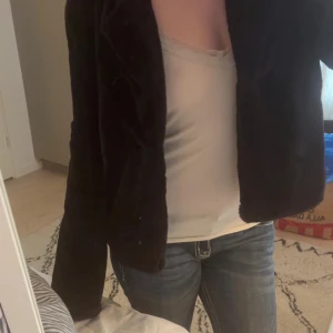 Svart pälsjacka med krage - Mysig svart pälsjacka med bred krage. Jackan har en enkel, stilren look som passar perfekt till jeans eller kjol. Den är fluffig och ger en trendig vibe, perfekt för kyligare dagar.