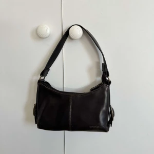 Brun vintage axelväska  - Snygg mörkbrun axelväska i äkta skinn köpt på second hand. Väskan har en vintage look med diskreta sömmar, guld detaljer och ett extra fack med dragkedja på baksidan. Perfekt storlek och passar till många olika outfits 💕 Priset kan diskuteras, skriv gärna vid funderingar! 