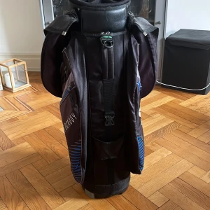 Motocaddy golfbag Club Series blå/svart - Säljer en Motocaddy Club Series golfbag i svart och blått med flera rymliga fack och dragkedjor. Väskan har tydliga loggor, praktiska fickor och detaljer i blått. Perfekt för att organisera golfutrustningen på banan. Köpt för runt 3500kr