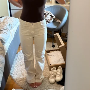 Vita bootcut jeans med fickor - Säljer ett par snygga vita jeans med bootcut passform och stora fickor fram. Byxorna har en klassisk midja och är tillverkade i ett mjukt bomullsmaterial som sitter skönt. Perfekta för dig som gillar en clean och stilren look. Något slitna längst ner , där bak. 