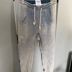 Ljusblå denimjoggers från ONE teaspoon  - Säljer ett par ljusblå denimjoggers från ONE teaspoon med elastisk midja och vit snörning. Byxorna har avslappnad passform, fickor fram och resår vid benslut. Perfekta för en chill och streetig look. Materialet är mjukt jeans och färgen är snyggt tvättad.