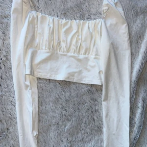Vit croppad långärmad topp - Snygg vit croppad topp med långa ärmar och rynkade detaljer över bysten. Aldrig använd