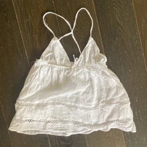 Vit linnetopp från Gina Tricot - Supersöt vit linnetopp från Gina Tricot med tunna axelband som korsas i ryggen. Toppen har broderade spetsdetaljer och en luftig passform.