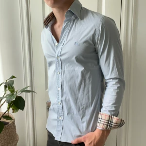 Burberry skjorta  - Ljusblå burberry skjorta. Modellen bär S och är 180,75 kg. Defekter: svettfläckar under båda armarna som ni ser på bild. De syns vid rött vinklar, vid kragen finns det minimal missfärgning från skulle gissa solkräm. Kom med frågor! Bra pris 🏆 