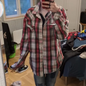 Rutig skjorta från Lee i bomull - Säljer en oversized rutig skjorta från Lee i storlek L. Skjortan har röda, vita, gröna och blå toner, klassisk krage och knäppning framtill. Tillverkad i mjuk bomull och har två bröstfickor med lock. Perfekt för en avslappnad och cool stil.