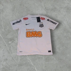 Vit Santos Neymar JR fotbollströja Nike - Snygg vit Santos fotbollströja från Nike med Neymar JR och nummer 11 på ryggen. Tröjan har korta ärmar, rund hals och flera tryck som BMG, Netshoes och Seara. Tillverkad i lätt Dri-FIT material som andas, perfekt för match eller träning.