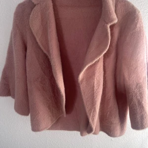 Rosa teddyjacka med krage - Supermjuk och fluffig teddyjacka i ljusrosa med bred krage och croppad passform. Jackan har en oversized look och är perfekt för dig som vill ha en cozy vibe. Materialet är pälsliknande och ger en riktigt mysig känsla.