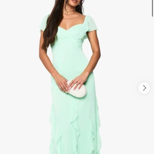 Mintgrön långklänning med volanger - Superfin mintgrön långklänning med korta ärmar och v-ringad hals. Klänningen har volangdetaljer längs kjolen som ger en flowig och drömmig känsla. Perfekt för dig som vill sticka ut med en ljus och fräsch look. Materialet känns lätt och luftigt. Aldrig använt så klänningen är i nyskick med prislapp kvar 