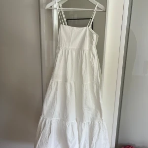 Vit långklänning med smala axelband - Säljer en vit långklänning med smala axelband och volangdetaljer. Smock i ryggen. Från MILO’S Paris, storlek S/M. Aldrig använd men köpt begagnad, är dock i väldigt fint skick och ser ny ut. Väldigt somrig och söt klänning! 