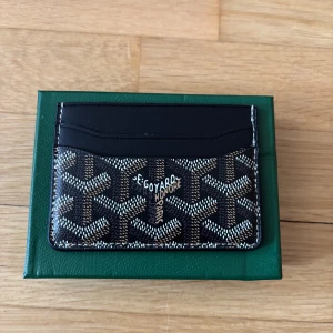 Goy4rd plånbok - Snyggt och stilrent kortfodral i svart skinn med deras ikoniska grafiska mönster i vitt och brunt. Perfekt för kort och ID, smidig att ha i fickan. Kommer i original grön ask med logga.