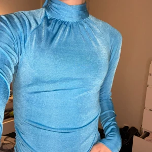 Blå långärmad polotopp från NA-KD - Säljer en blå långärmad polotopp från NA-KD i glansigt material. Toppen har öppen rygg med knyt i nacken och en tight passform som framhäver figuren. Använd bara fåtal gånget o säljs pga ingen användning!💕