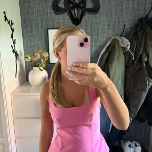 Rosa omlott topp med rosett - Säljer en superfin rosa topp med breda axelband och fyrkantig urringning. Toppen har en stor rosett och omlott-detalj i ryggen som ger en extra söt vibe. Modellen är croppad och har en lätt utsvängd form nedtill. Perfekt för dig som gillar färg och statement-plagg!