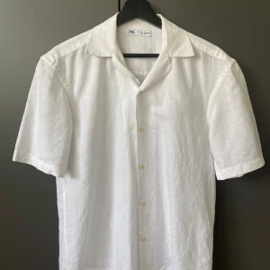 Vit linneskjorta från Zara, S - Fräsch vit skjorta från Zara i storlek S, tillverkad i linne. Skjortan har korta ärmar, klassisk krage och knäppning framtill med ljusa knappar. Perfekt för varma dagar och en clean look. Snyggt och enkelt plagg som funkar till jeans eller shorts.
