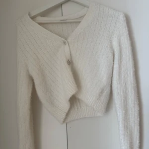 Vit kofta från Lindex med pärlknappar - Superfin vit kofta från Lindex med fluffig stickat material. Koftan har långa ärmar och flera dekorativa knappar med pärlor och strass! 