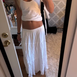 Vit långkjol från Stradivarius - Säljer en vit långkjol från Stradivarius med skön resår i midjan. Kjolen har en flowy och luftig känsla med lätt skrynklat tyg, perfekt för varma dagar. Enkel och stilren design som är lätt att matcha med olika toppar.