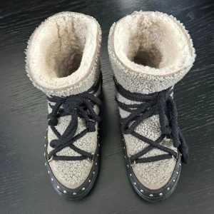  Inuikii curly rock i taupe strl.38 - Snygga boots från Inuikii i beige fårskinn med svarta o bruna detaljer och snörning. Skorna har svartabruna läderpartier med små nitar runt sulan och grova svarta snören. Perfekta för kalla dagar med sin fluffiga insida och coola look. Strl 38