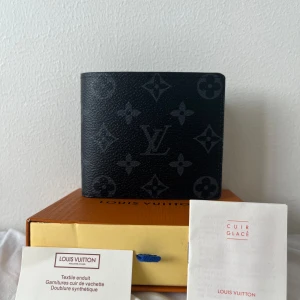 Svart luviton plånbok - Snygg svart plånbok från luviton med klassiskt monogrammönster i grått. Tillverkad i skinn med flera kortfack och stilren design. Perfekt accessoar för dig som vill ha något exklusivt och tidlöst i fickan.