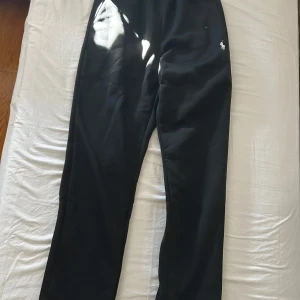 Svarta mjukisbyxor från Ralph Lauren - Svarta mjukisbyxor från Ralph Lauren med klassisk broderad logga i vitt på höften. Byxorna har elastisk midja och är gjorda i mjukt bomullsmaterial, perfekta för chill dagar eller när du vill vara bekväm men ändå se snygg ut.