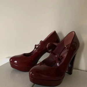 Vinröda lackpumps med rem - Säljer ett par vinröda pumps i glansigt lackmaterial med rund tå och hög klack. Skorna har en smal rem över foten som ger en klassisk Mary Jane-look. Ganska små i storleken så skulle tipsa om att köpa dem om man har storlek 36…💕