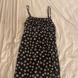 Svart blommig sommarklänning - Supersöt svart kortklänning med smala axelband och vita blommor med gula detaljer