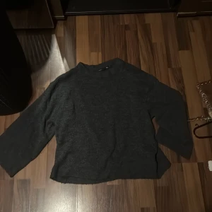 Mörkgrå stickad tröja med trekvartsärm - Mysig mörkgrå stickad tröja med avslappnad passform och trekvartsärmar. Perfekt för lager-på-lager och chill dagar. Enkel design som funkar till det mesta och är lätt att matcha med jeans eller kjol.