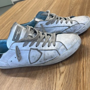 Vita Philippe Model sneakers i skinn - Snygga vita sneakers från Philippe Model med grå snörning och detaljer. Skorna har en klassisk låg profil, rund tå och är tillverkade i skinn med ljusblå insida. Perfekta för dig som gillar en stilren och urban look. Har box. Hör av er vid minsta fråga!🤩