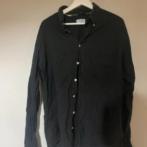 Svart skjorta från Eton, slim fit XL - Svart långärmad skjorta från Eton i slim fit-modell, storlek XL (43). Skjortan har klassisk krage med knappar och är tillverkad i ett mjukt bomullstyg. Perfekt för dig som gillar stilrena och enkla plagg med snygg passform.