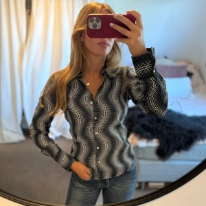 Svartvit skjorta med vågigt prickmönster - Snygg svart skjorta från SIS by Sisters Point med vågigt mönster av vita prickar. Skjortan har klassisk krage, knappar framtill och långa ärmar