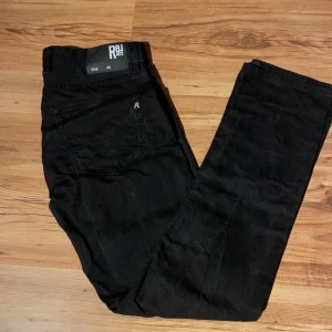 Svarta jeans från Replay RBJ - Svarta jeans från Replay RBJ med klassisk femficksdesign och raka ben. Jeansen har en stilren look med diskret logga på bakfickan och är tillverkade i ett mjukt bomullsmaterial med lite stretch för extra komfort.