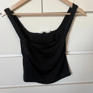 Svart linnetopp från NA-KD XS - Säljer en svart linnetopp från NA-KD i storlek XS. Toppen har breda axelband och en enkel, stilren design som är lätt att matcha. Perfekt för varma dagar eller att styla lager på lager. Materialet känns mjukt och följsamt mot huden.