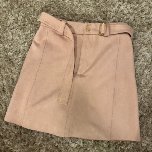 Ljusrosa mockakjol från Zara XS - Supersnygg ljusrosa kortkjol från Zara i mjuk mocka-look. Kjolen har ett matchande bälte med guldfärgat spänne och knapp framtill. Köpte nyligen och har använts 1 gång. 💕