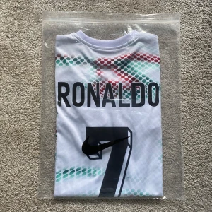 Portugal Ronaldo 7 fotbollströja Puma - Portugal landslagströja från Puma med Ronaldo 7 på ryggen. Vit bas med prickigt mönster i rött, blått och grönt. Kortärmad modell med svarta detaljer vid ärmslut och krage. Tillverkad i lätt och ventilerande funktionsmaterial.