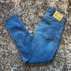 Blå Replay Anbass jeans  - Säljer ett par klassiska blå Replay Anbass jeans med raka ben och snygg tvätt. Jeansen har fem fickor, dragkedjegylf och Replay-logga på bakfickan samt läderpatch i midjan. Tillverkade i mjukt denim för skön passform. Köpta för 1000 kr på Zalando och är i väldigt bra skick och nästan aldrig använda. Jeansen är i storlek 27/30 och är försmå för mig som är 177 cm. Perfekt inför hösten!