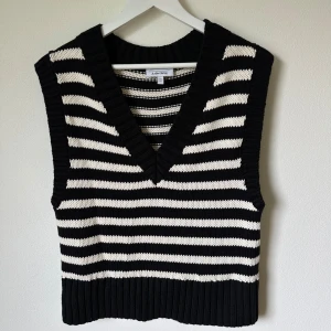 Randig stickad väst från & Other Stories - Snygg stickad väst från & Other Stories i svart och vitt med breda ränder. Modellen har v-ringning och ribbade kanter. Tillverkad i 100% bomull, perfekt att styla över en skjorta eller t-shirt för en trendig look. 1F17