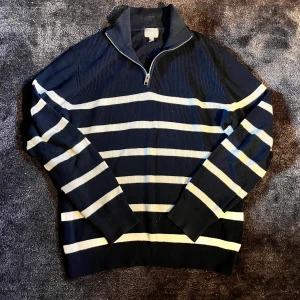 Marinblå randig half zip tröja - Använd fåtal gånger. Är storlek S men passar mer som en M. Säljer en snygg marinblå stickad tröja från Ami med vita horisontella ränder. Tröjan har en half zip-dragkedja vid halsen och ribbade muddar. Perfekt för dig som gillar klassisk stil med en modern touch.