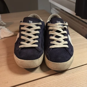 Mörkblå sneakers från The Last Conspiracy - Snygga mörkblå the gallerist sneakers i mocka med vita detaljer och snörning. Skorna har lite slitningar som ni ser på bilden men är riktigt snygga för dig som vill sticka ut pris är inte hugget i sten hör av er om ni är intresserade 