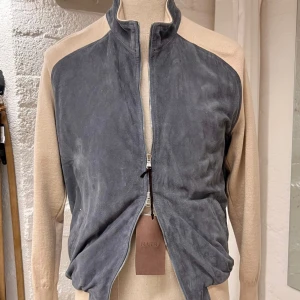 Barba mockajacka med beige ärmar - Snygg jacka från Barba Napoli med blå mocka framtill och baktill samt kontrasterande beige ärmar stickade i ”virgin wool”. Jackan har hög krage, dragkedja och en clean, sportig look. Perfekt för dig som gillar stilrena detaljer och mjuka material. Storlek 50 passar mer som 48 skulle jag säga. Sitter bra på mig som bär M. Retail 900€.
