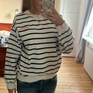 Randig sweatshirt med brodyr - Vit och svart randig sweatshirt med broderad text 'perdu mon coeur à paris' i rött på bröstet. Tröjan har rund hals, långa ärmar och ribbade muddar. Perfekt för en chill och stilren look. Storleken är s. 