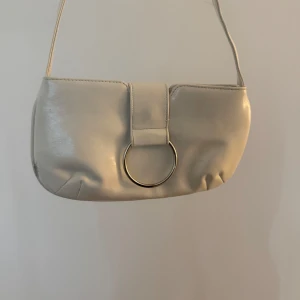 Beige axelväska med metallring - Snygg beige axelväska i skinnimitation med stilren design och en stor silverfärgad metallring framtill🤍