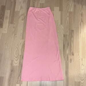 Ljusrosa långkjol i bomull - Säljer en enkel och snygg ljusrosa långkjol med rak passform. Kjolen har resår i midjan och är gjord i mjukt bomullstyg som känns skönt mot huden. Perfekt för dig som gillar minimalistisk stil och vill ha en chill look. Passar XS och S