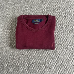 Vinröd tröja från Polo Ralph Lauren - Snygg vinröd tröja från Polo Ralph Lauren i mjuk pima bomull. Klassisk rund hals och långärmad modell med broderad logga på bröstet. Perfekt för dig som gillar stilrena och tidlösa plagg med skön passform.