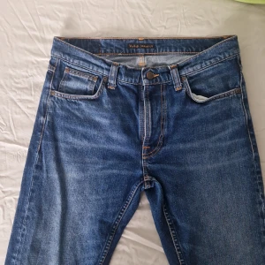 Nudie Jeans W31 L32 - Säljer ett par blå jeans från Nudie Jeans Co i storlek W31 L32. Jeansen har snygga kontrastsömmar, fem fickor och Nudie-logga på bakfickan. Tillverkade i slitstarkt bomullstyg.Jeansen är slim fit modell lean dean. Säljer dom för att dom inte passar mig.