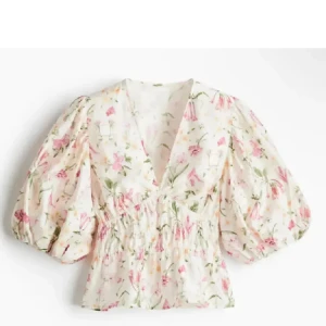 Blommig blus med puffärm - Supersöt blommig blus med v-ringning och  puffärmar. Blusen har smockad midja och är täckt av rosa och gröna blommor på vit botten. Perfekt för dig som gillar romantisk och trendig stil.